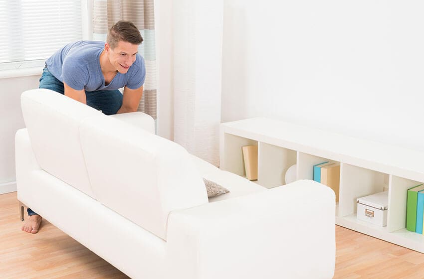 The image depicts a residential driveway scene in Hyde Park with a focus on a large, open-top waste container filled with assorted rubbish. The container appears to be made of metal, painted in a neutral grey, and shows visible signs of use, including some surface scratches and minor rust spots. It is situated on a paved driveway area, with its front side partially facing the viewer, allowing a clear view of the varied waste items inside. Among the contents are several black bin bags, crumpled cardboard boxes, a plastic container, and some loose debris, suggesting household or light commercial waste. To the right of the container, a portion of a white panel van is visible, with part of the vehicle's side door and a wheel showing, indicating that it is parked close by for waste collection. The background reveals a suburban residential setting with a section of a brick house and a small garden area, typical of Hyde Park properties. The lighting is diffuse, indicating an overcast day, which softens shadows and highlights the textures of the waste and the vehicle. The scene aligns with rubbish removal services provided by Hire Man and Van in the W2 postcode area, demonstrating a typical waste clearance operation in a local residential context.